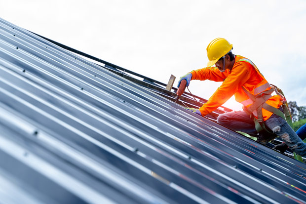 Roofer worker in protective uniform wear and gloves, using air or pneumatic nail gun and installing asphalt shingle on top of the new roof,Concept of residential building under construction.